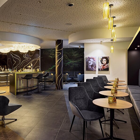 Hotelbar mit runden Tischen, dunklen Stühlen und moderner grün-grauer Theke