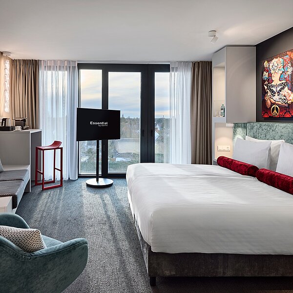 Modernes Hotelzimmer mit Doppelbett und Details in türkis, grau und rot sowie Sitzbank, Sessel, Wasserkocher und Nespressomaschine